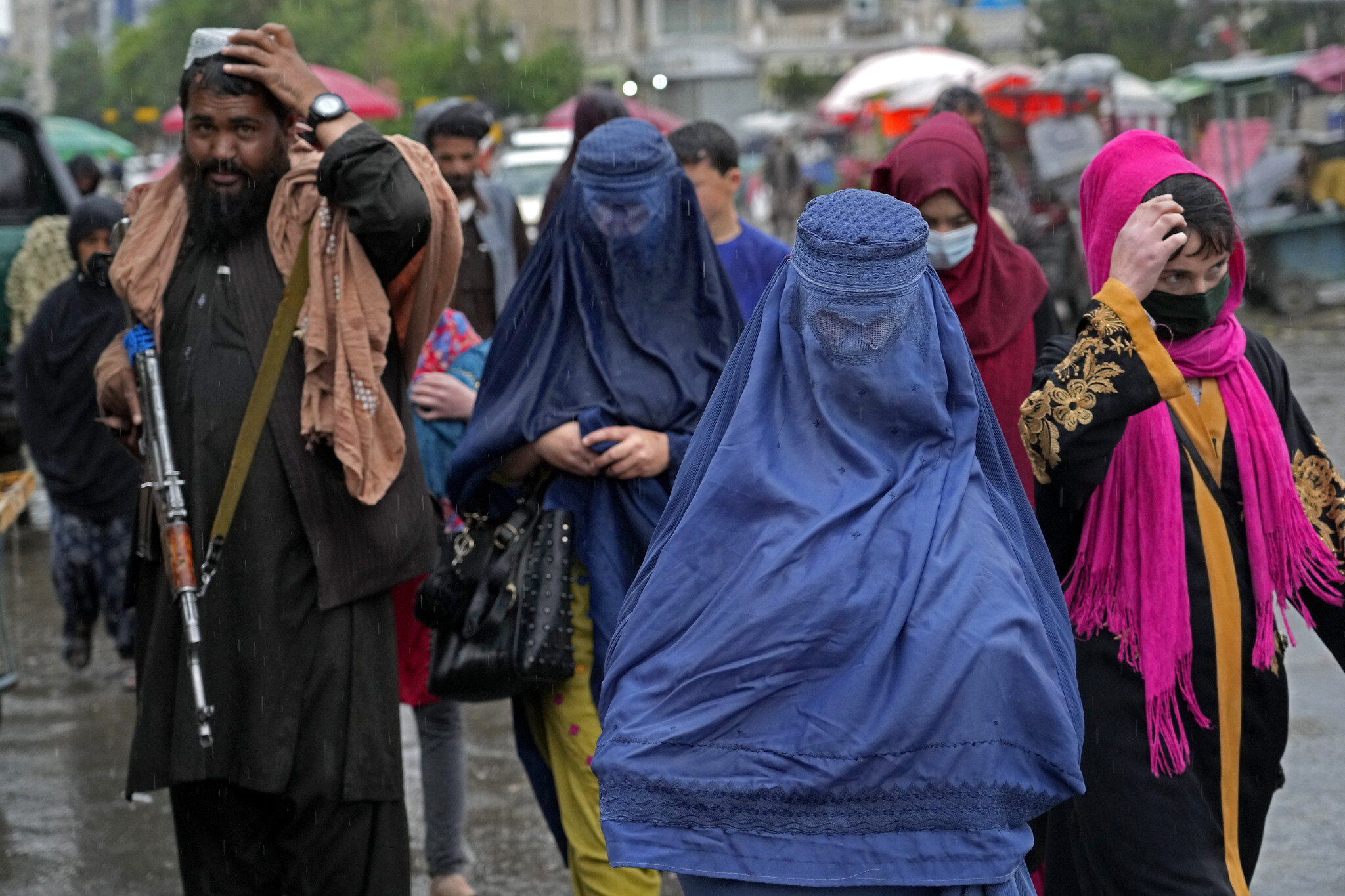 Afghan women walk through the old market as a Taliban fighter stands guard, in downtown Kabul, Afghanistan, Tuesday, May 3, 2022. Afghanistan’s Taliban rulers on Saturday, May 7,  ordered all Afghan women to wear head-to-toe clothing in public, a sharp hard-line pivot that confirmed the worst fears of rights activists and was bound to further complicate Taliban dealings with an already distrustful international community.(AP Photo/Ebrahim Noroozi)